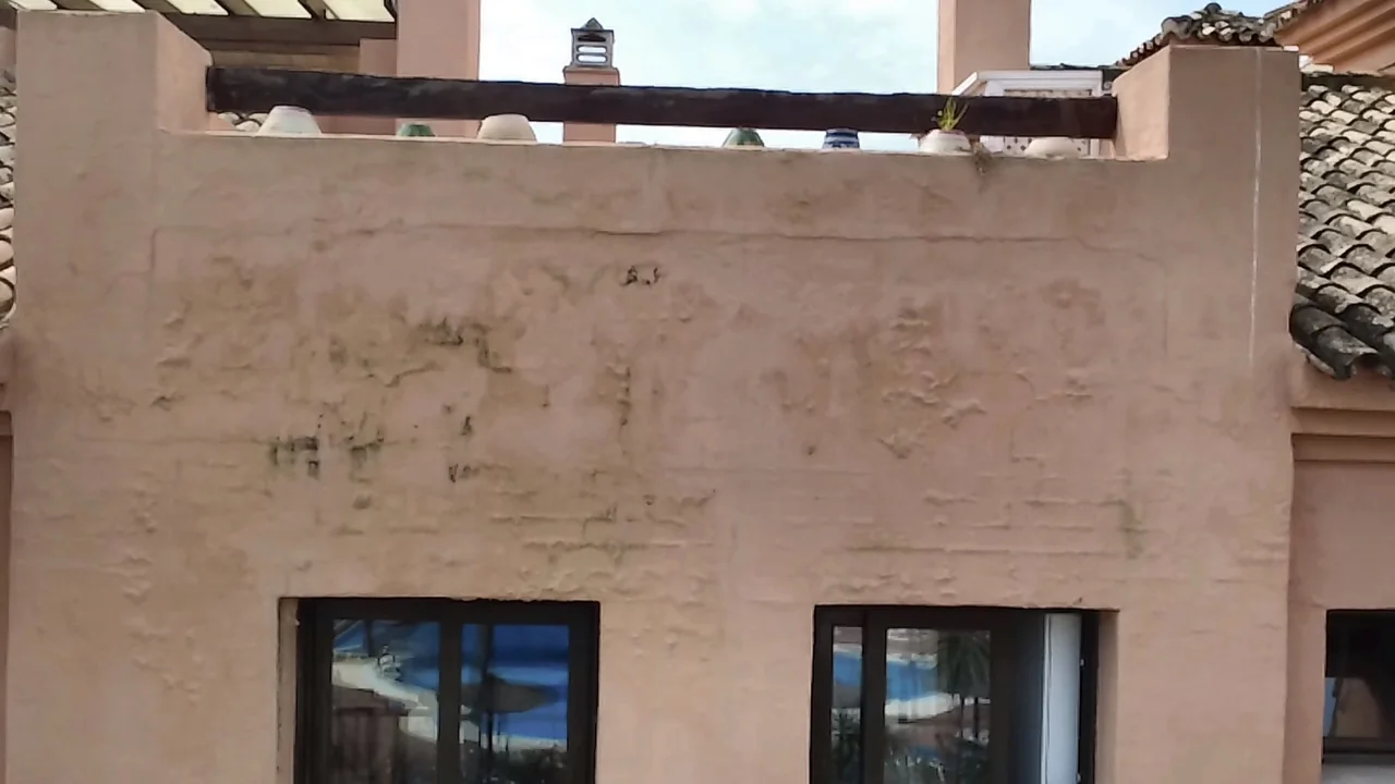 Fachada con abolsamiento de pintura, desconchados y manchas bajo el peto de una terraza